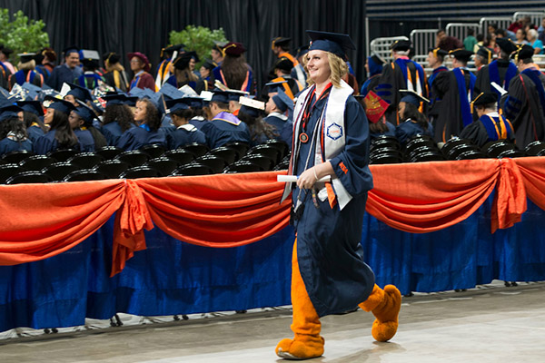 UTSA graduate walking during commencement while wearing roadrunner costume legs