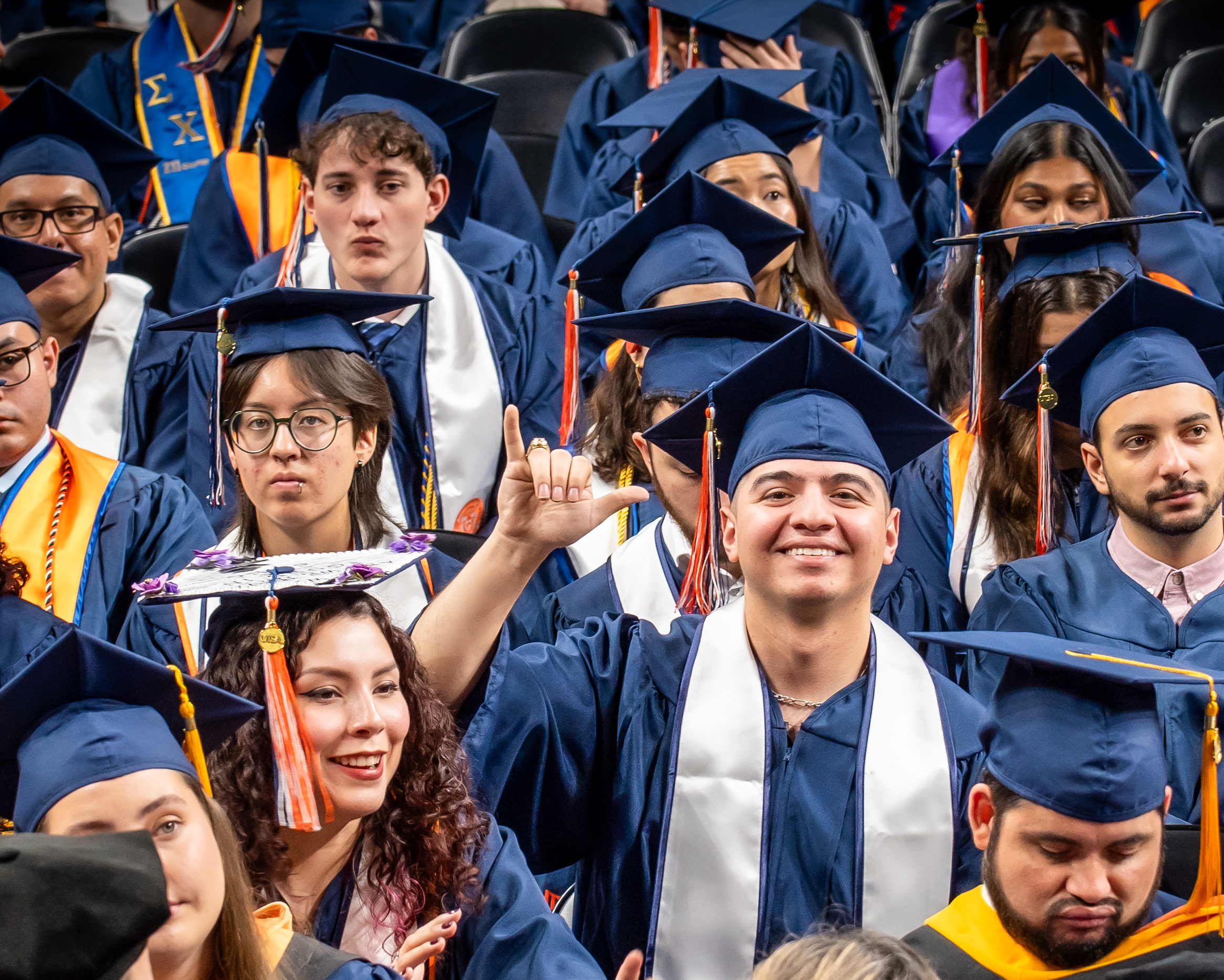 Crowd of UTSA graduates in cap and gown posing and holding the UTSA birds up photo