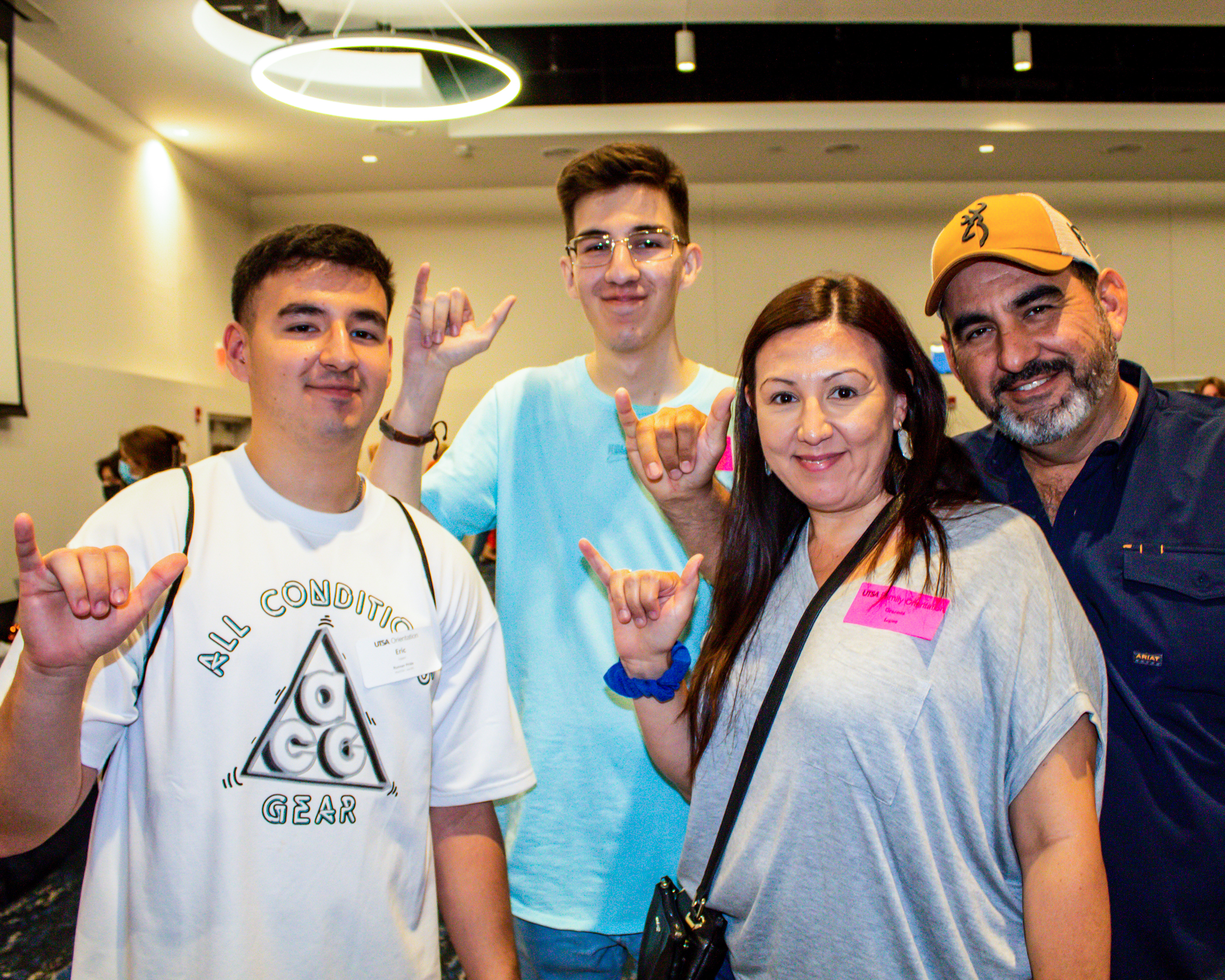 Two future students posing with the birds up hand pose with their parents also doing the birds up hand gesture