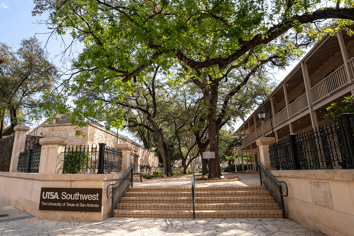 Tall trees and a sign on the wall for the Southwest campus with steps leading up to a stone building.