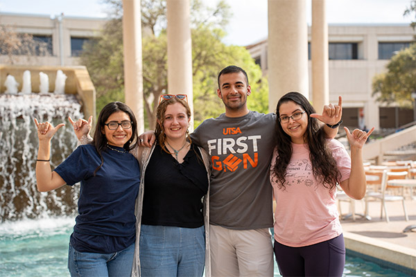 Four students taking a picture at the Sobrilla fountain giving the birds up sign